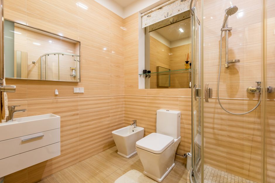 Interior of modern bathroom with light orange walls and white sink under mirror near toilet and bidet next to shower cabin