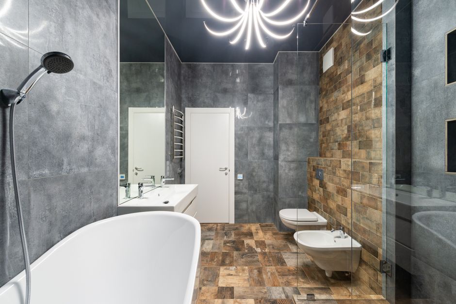 Interior of contemporary bathroom with bathtub and shower next to sink with tap under mirror in front of bidet and toilet near door
