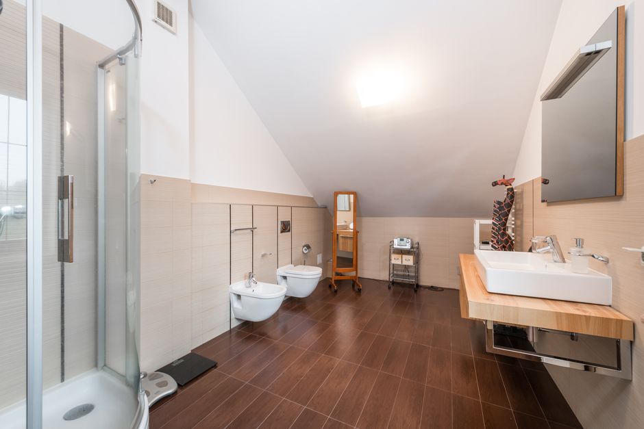 Minimalistic design interior of contemporary spacious bathroom with glass shower cabin next to bidet and toilet near sink with mirror in modern house